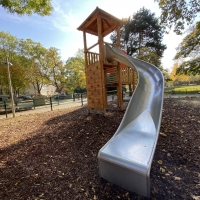 Hoher Spielturm mit Kletterwand und lange silberne Rutsche