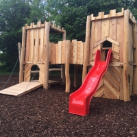 Spielplatz mit Burganlage aus Holz mit roter Rutsche