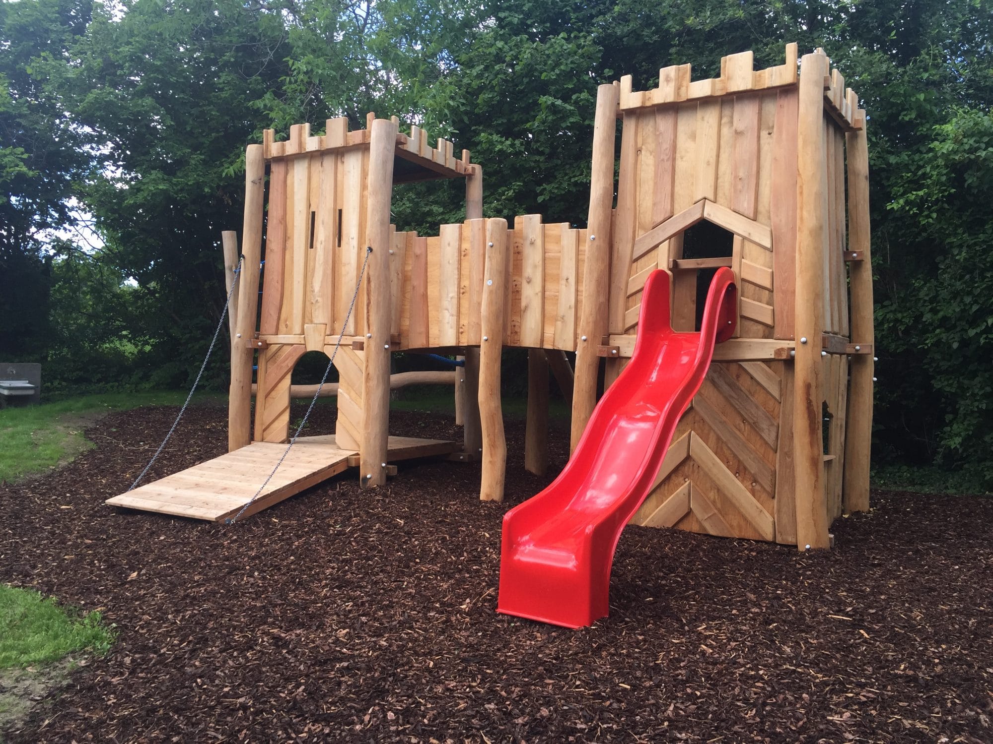 Spielplatz mit Burganlage aus Holz mit roter Rutsche