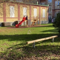 Kletterturm mit roter Kunststoffrutsche und einem Balancierbalken