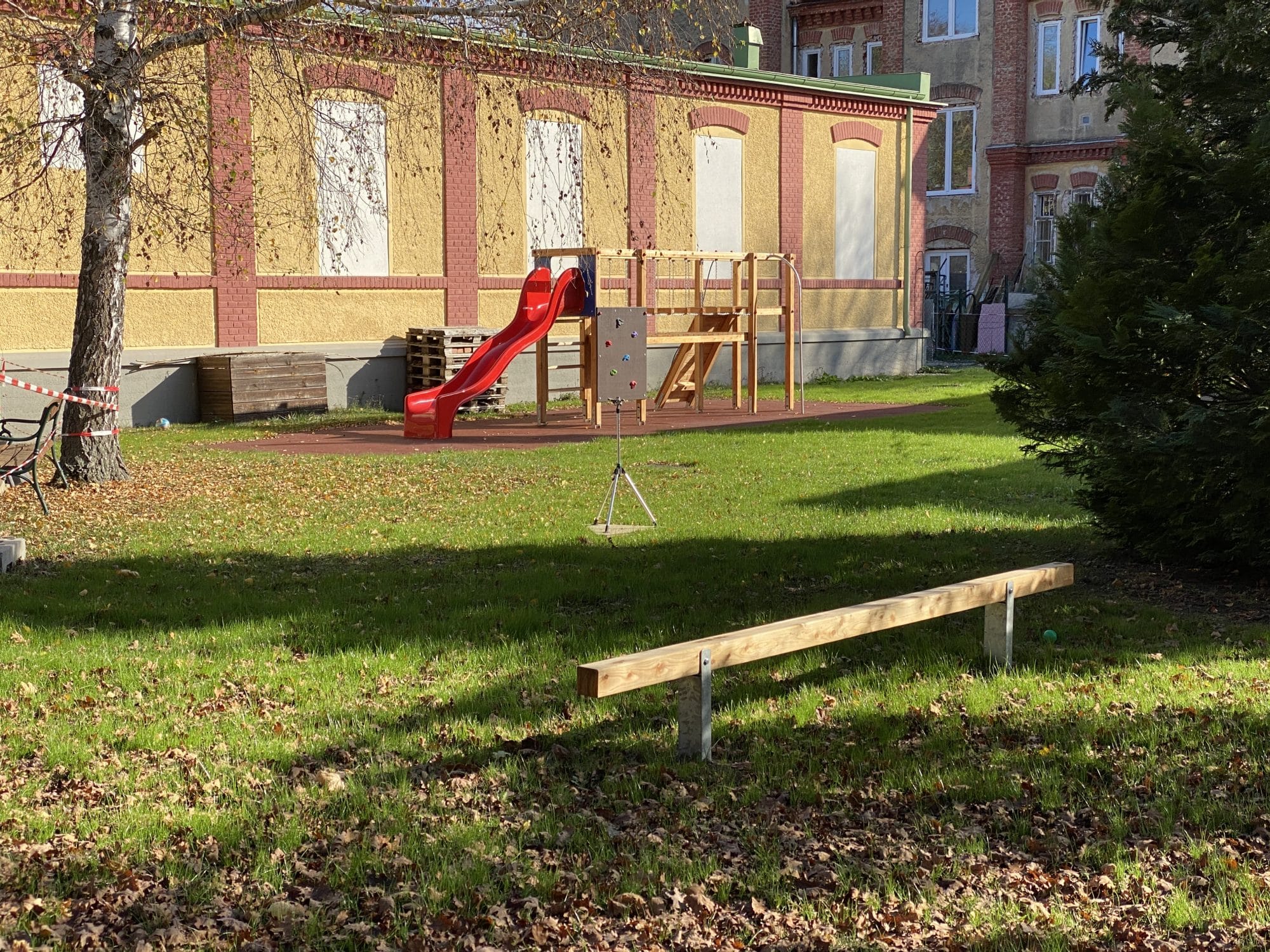 Kletterturm mit roter Kunststoffrutsche und einem Balancierbalken